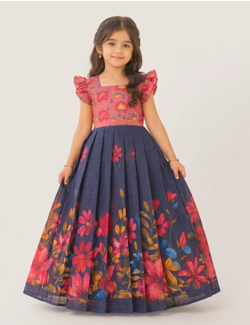 A young girl modeling a traditional Indian salwar kameez dress with a navy blue flared skirt and a pink floral bodice, set against a plain light gray background.