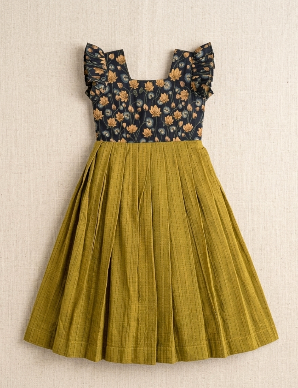 A sleeveless dress with a dark navy floral bodice and ruffled cap sleeves, paired with a pleated olive green skirt, displayed flat against a textured beige background.
